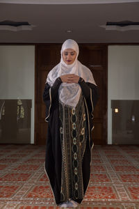 Full length of woman in burka praying while standing on carpet