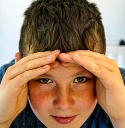 Close-up portrait of boy looking through his hands , freckles , cheeky 