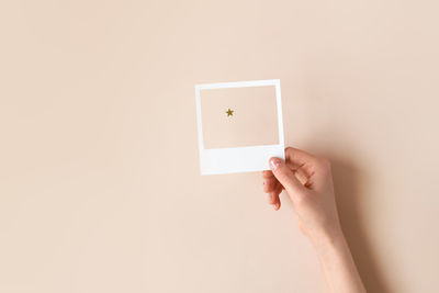 Female hand holding a white paper frame with a star seen through it on beige background