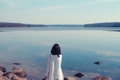 Rear view of woman standing by lake against sky