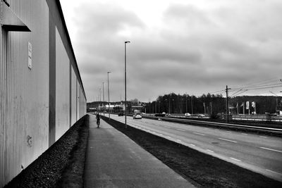 Road passing through city against cloudy sky