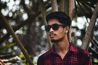 Young man wearing sunglasses looking away while standing outdoors