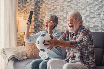 Friends using mobile phone while sitting on sofa at home