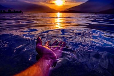 Low section of person on sea at sunset