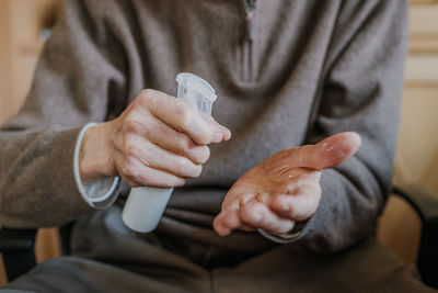 Midsection of senior man using hand sanitizer at home