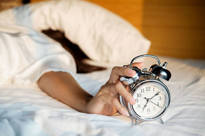 Woman snoozing alarm clock on bed at home
