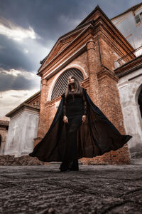 Low angle view of woman standing by building against sky