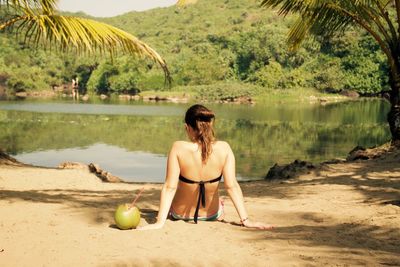 Rear view of woman sitting on beach against sky