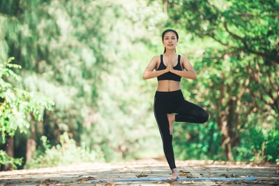 Full length portrait of young woman practicing yoga in tree position at park