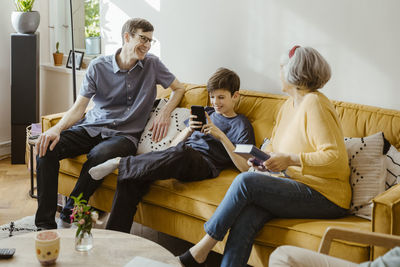 Happy man sitting on sofa with son and mother-in-law at home