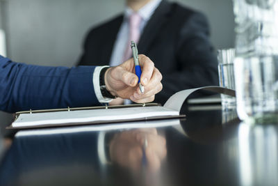 Midsection of businessman holding pen over paper by colleague in office