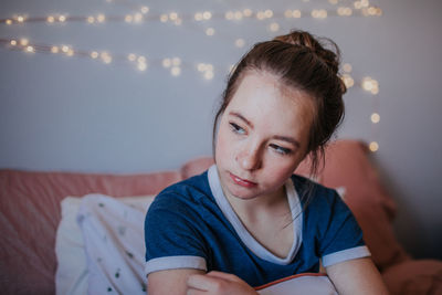 Portrait of tween girl sitting on bed looking away