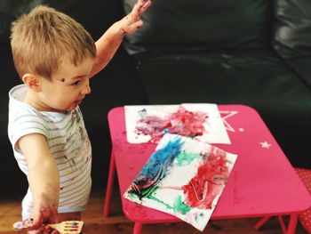 Side view of baby boy with messy hands standing by pink table at home