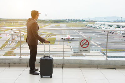 Rear view of man standing at airport against sky