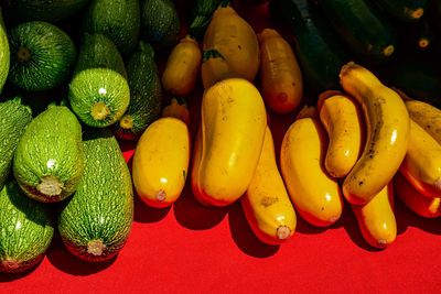 Yellow and green squash stacked on red cloth in vendor stall at farmer's market