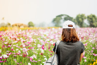 Rear view of woman standing by flowering plants against sky