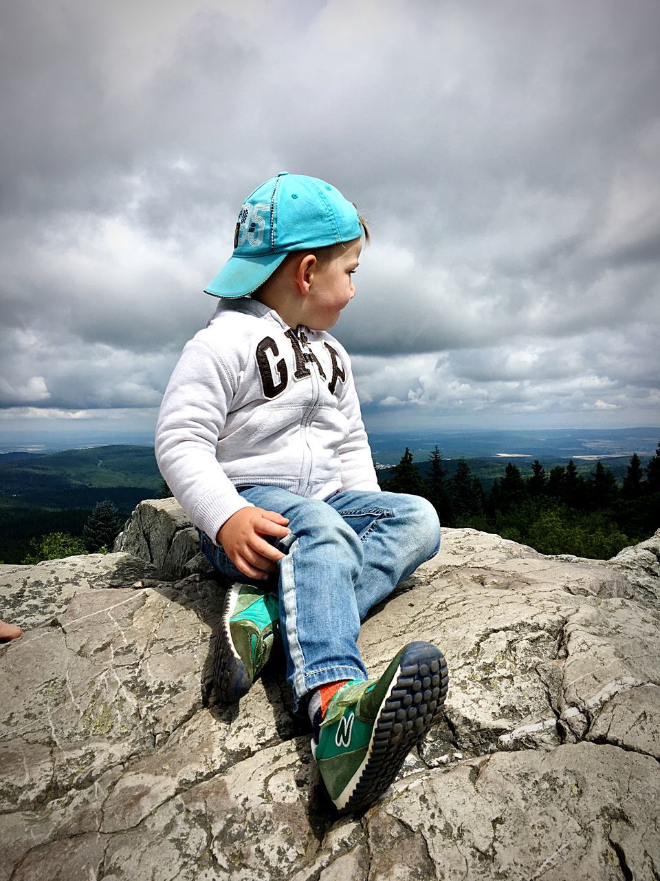 childhood, boys, cloud - sky, real people, one person, casual clothing, full length, sky, rock - object, leisure activity, elementary age, sitting, day, outdoors, lifestyles, shoe, adventure, one boy only, nature, beauty in nature, water, people