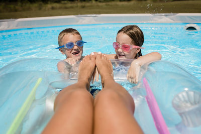 Mother floats on raft in pool with kids splashing at feet on sunny day