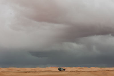 Baby blue jeep drives on sand dunes of utah desert under stormy skies