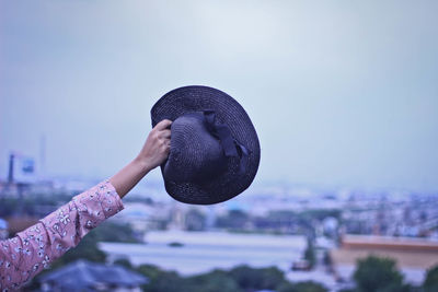 Close-up of person holding hat against sky