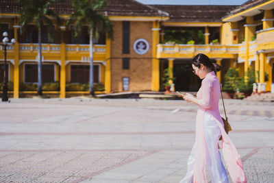 Woman with vietnam culture traditional dress using smartphone at street in hoi an.