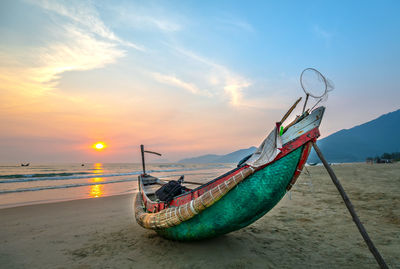 Fishing boat on beach against sky during sunset