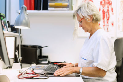 Side view of senior orthopedic surgeon using computer at desk in clinic