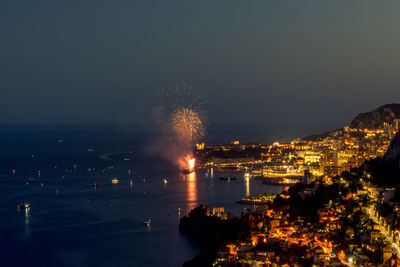 Illuminated city by sea against sky at night