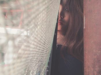 Close-up portrait of woman standing by curtain of window