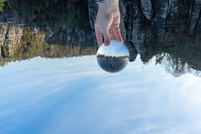 Upside down image of cropped hand holding crystal ball with reflection