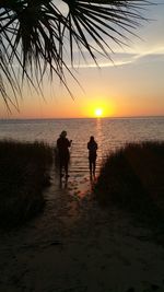 Silhouette people walking on beach against sky during sunset