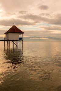 Lifeguard hut in sea against sky during sunset