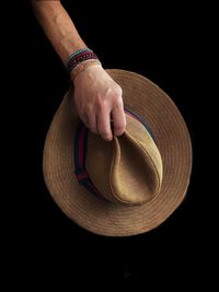 Close-up of man holding hat against black background