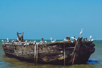 Abandoned boat moored in sea against clear blue sky