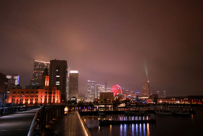 Illuminated buildings by river against sky in city at night