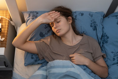 Cute woman lying in bed, holding hand on head and suffer from heat temperature. girl feeling bad