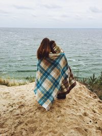 Rear view of couple covered with blanket standing by sea on rock