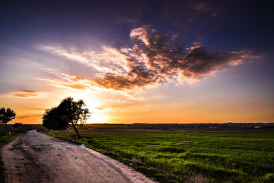 Road amidst field against sky during sunset