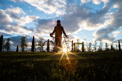 Man riding bicycle on field against sky during sunset