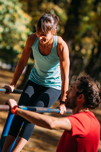 Woman exercising on parallel bar in the park with personal trainer