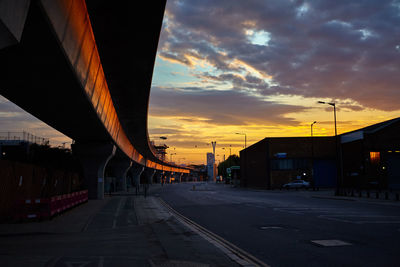 Road by bridge in city against sky during sunset