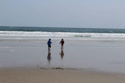 Boys walking on shore at beach against clear sky