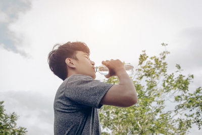 Rear view of boy drinking against trees and sky