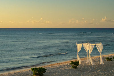 Scenic view of beach against sky during sunset. white fabric drapped trelles blows in the wind. 