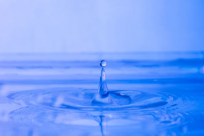 Close-up of drop splashing on water against blue background