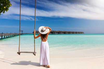 Rear view of woman standing by swing at beach