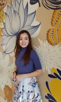 Portrait of smiling young woman standing against wall