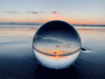 Close-up of water on beach against sky during sunset with lense ball
