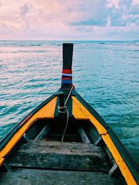 Longtail boat on sea against cloudy sky