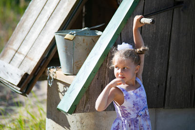 Surprised pretty little girl in country style staying near to well.